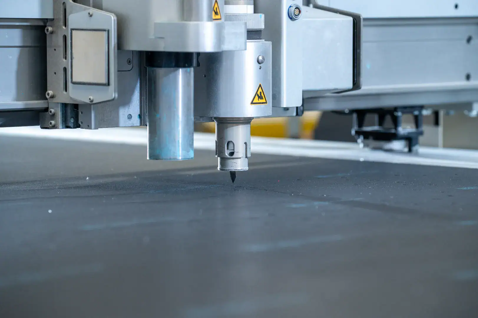 Close-up of a CNC cutting head working on a sheet of grey material.