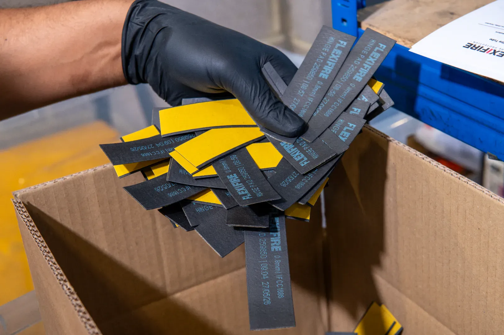 Black-gloved hand placing Flexifire material offcuts into a cardboard box.