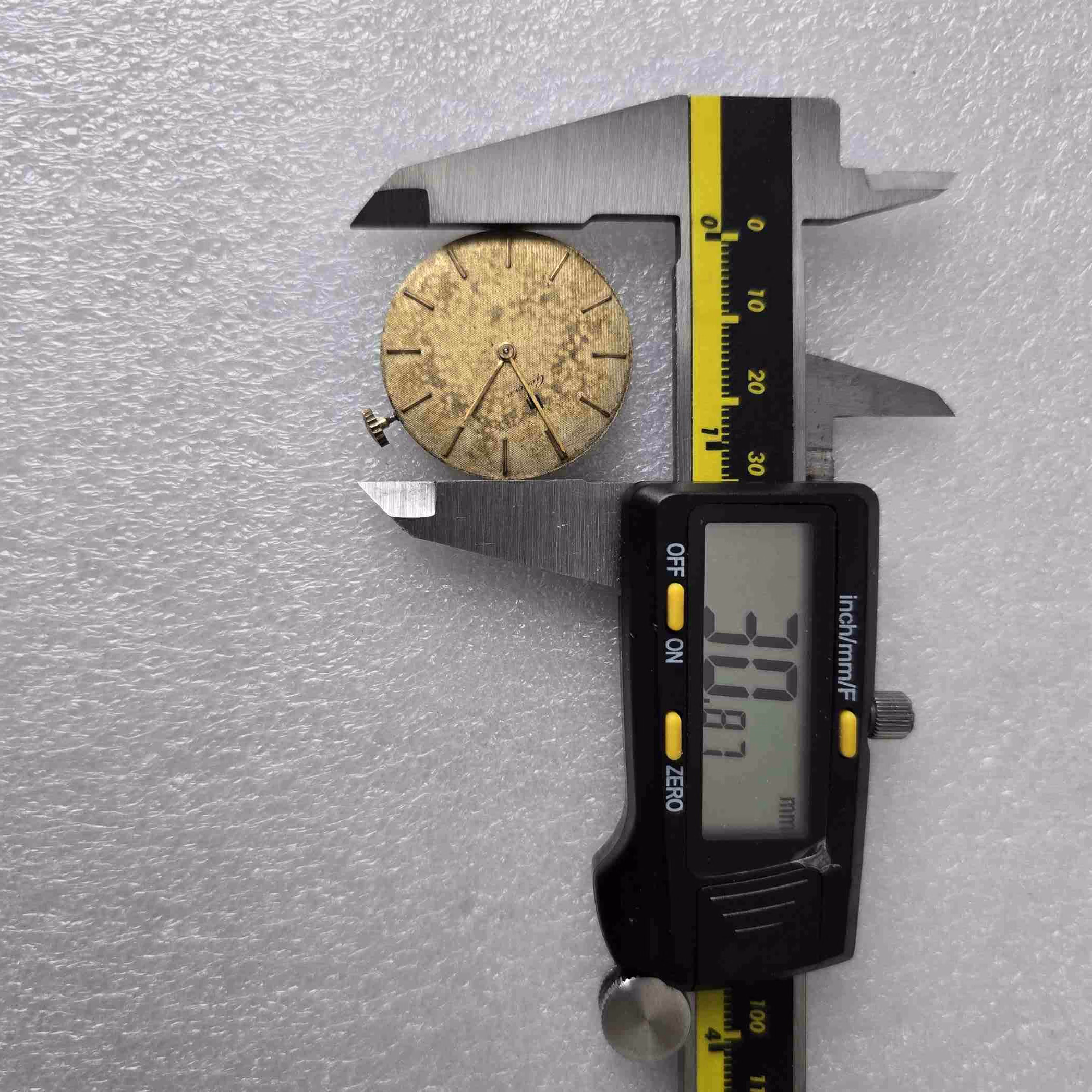 Caliper measuring a round gold watch face, showing measurement in millimeters on the scale.