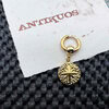 Gold earring with textured round pendant on paper.