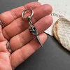 Hand holding silver skull keyring on grey surface.