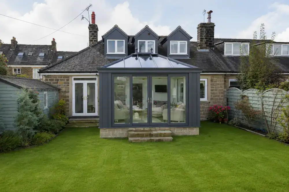 Conservatory {location} with anthracite frames, glazed roof lantern, French doors and stone base walls opening onto a garden.
