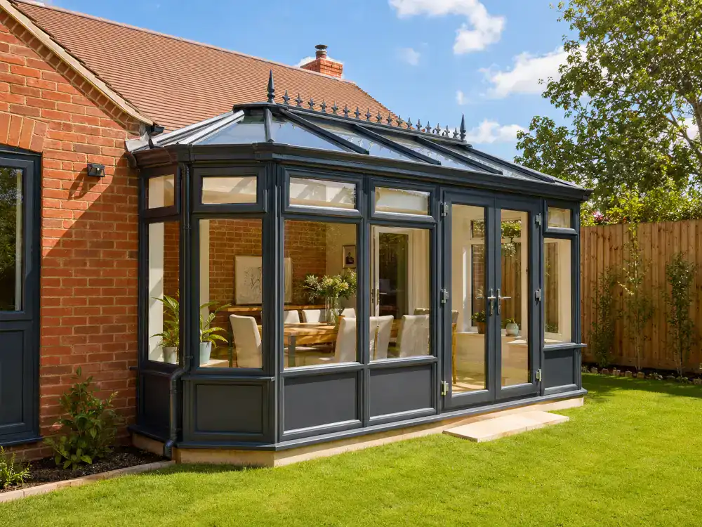 Conservatory with anthracite frames, decorative glazed roof, French doors and a bright dining area attached to a brick home.