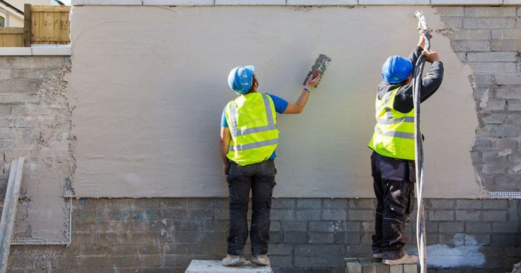 Workers applying cement plaster on exterior brick wall for smooth finish