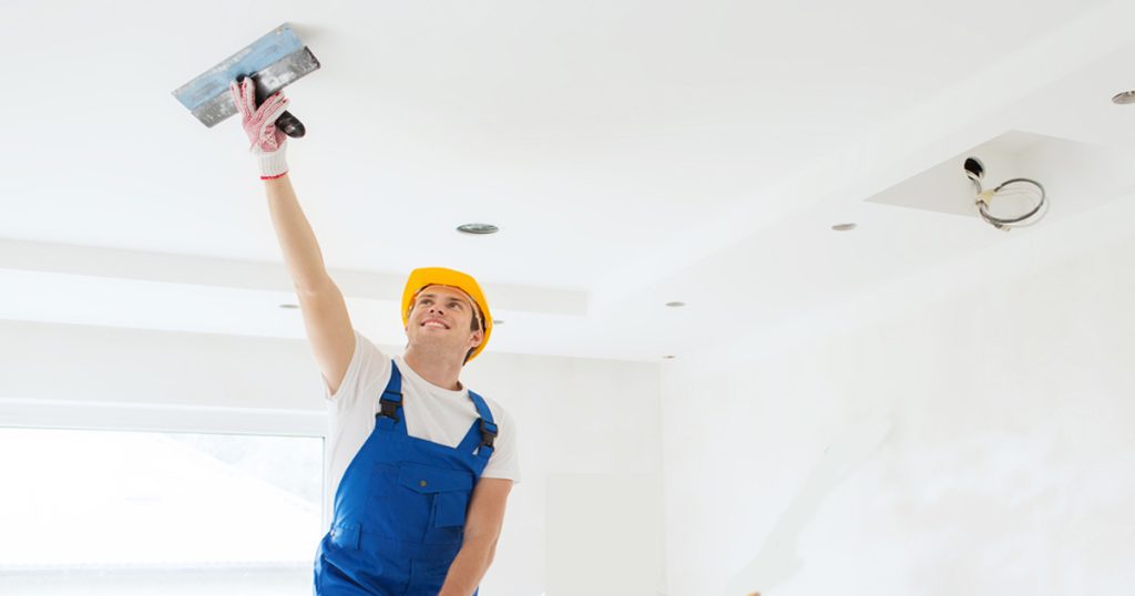 Worker applying wall putty on ceiling for smooth interior finishing