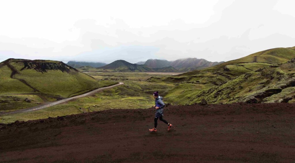 A photo of a man running through some green hills on a dirt track