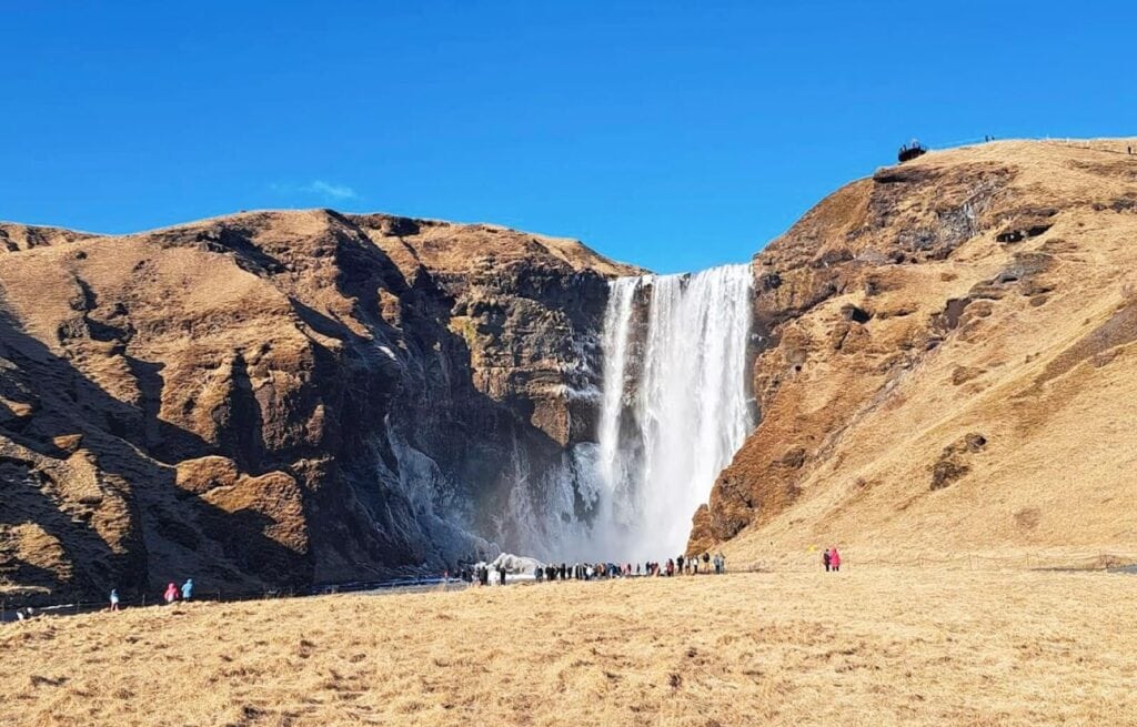 Skogafoss waterfall in winter with a clear blue sky and visitors at the base.