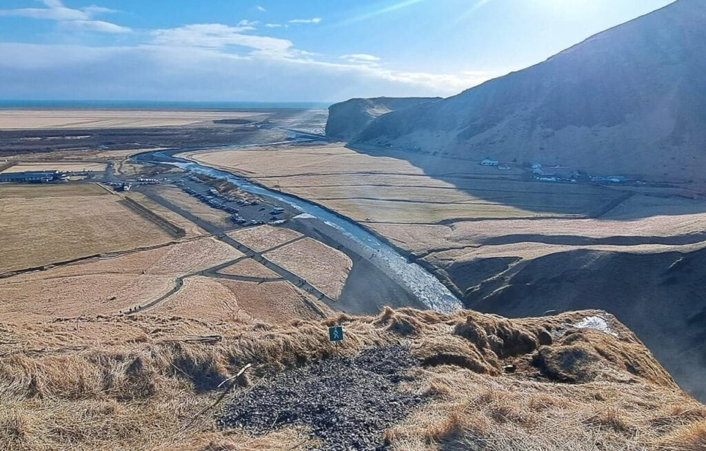 Wide view of a river flowing through a flat Icelandic valley with surrounding hills and distant mountains.