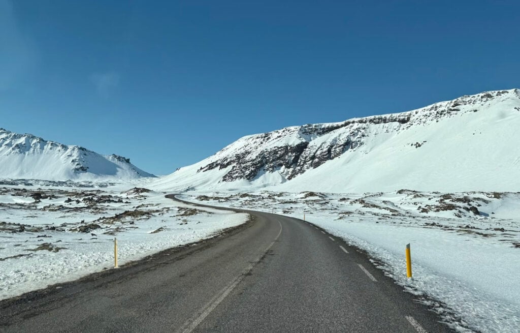 Snow-covered mountain landscape with a winding road and clear blue sky.