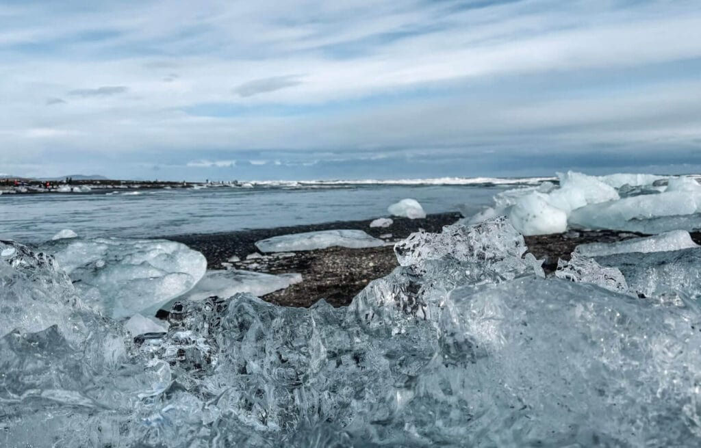 Ice chunks on a rocky shoreline with a distant view of the sea and cloudy sky in Iceland.