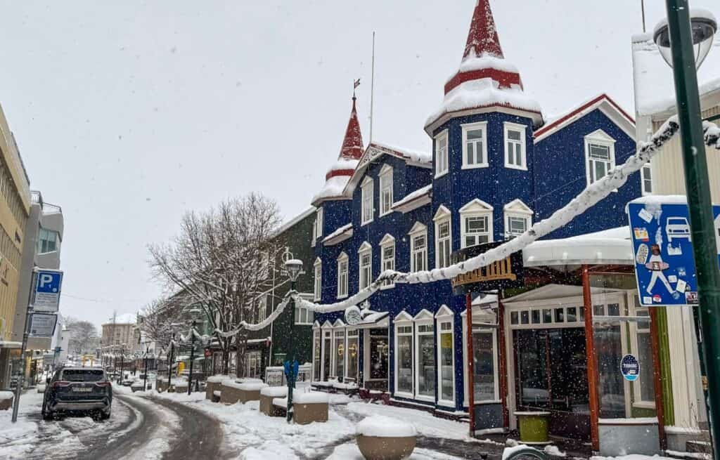 Snow-covered street with colourful blue building and red turrets in Akureyri during winter.