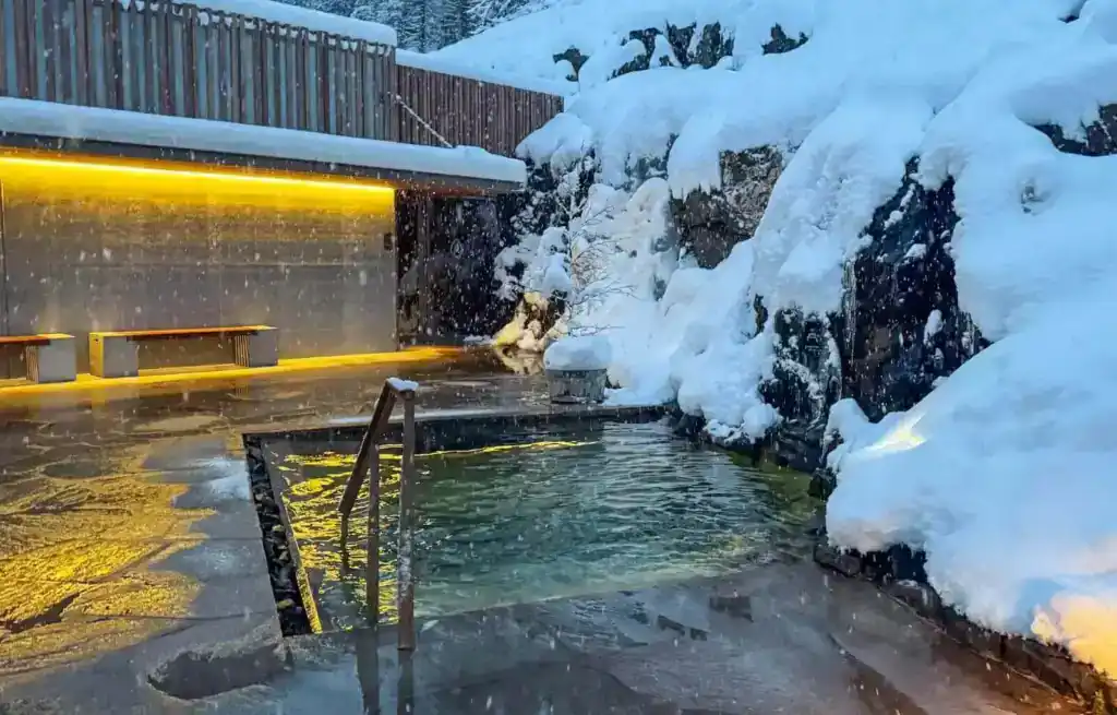 Snow-covered rocks and a hot tub with a metal handrail in a snowy landscape in Iceland.