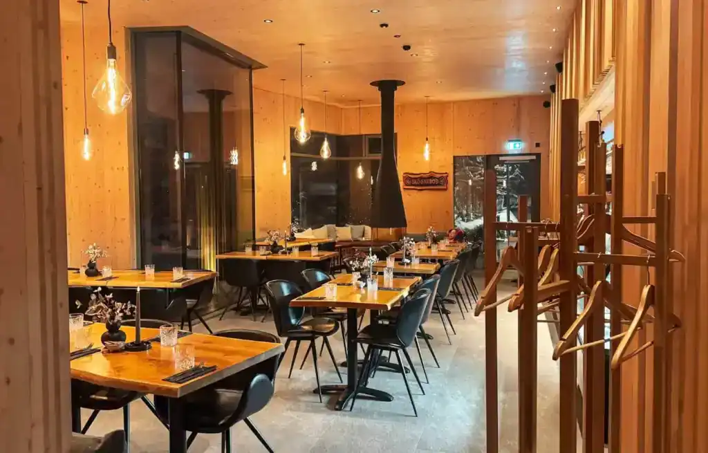 Interior of a cosy restaurant with wooden walls, black chairs, and tables set with flowers and glasses.