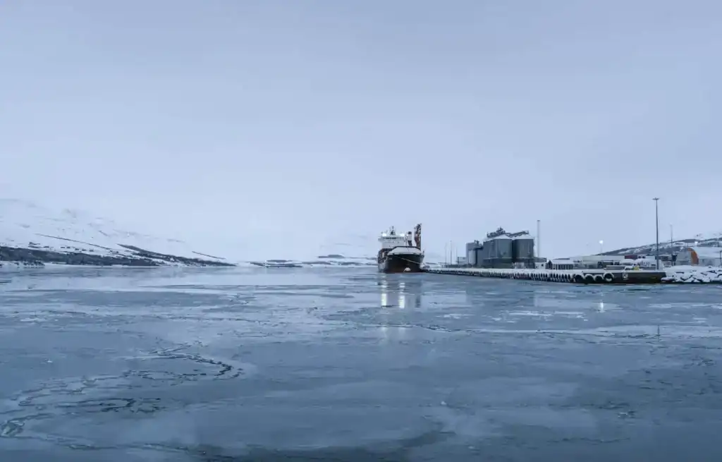 Frozen harbour with a ship docked and snow-covered landscape in Akureyri, Iceland.