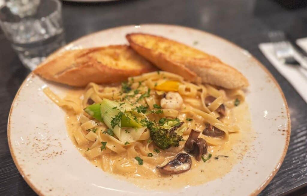 Creamy pasta with vegetables and garlic bread on a white plate.