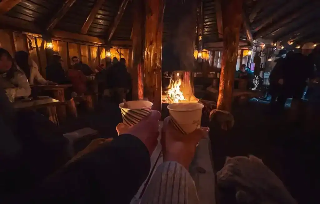 People relaxing around a fire inside a rustic wooden lodge in Tromso.