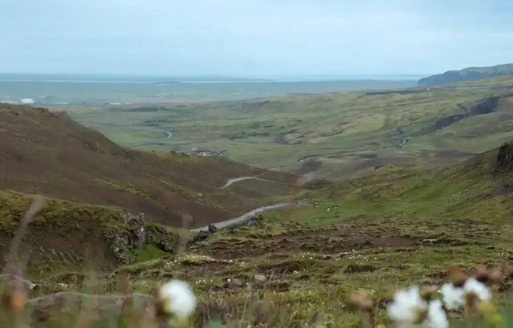 Wide view of rolling green hills and a winding road in a remote landscape with distant sea and sky.