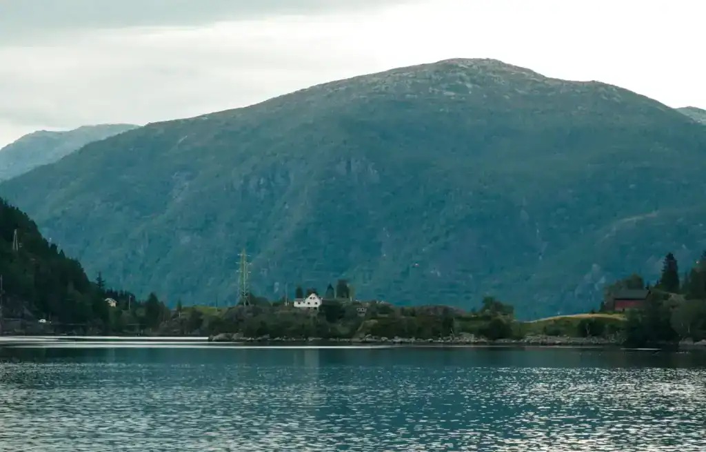 Scenic view of a large mountain behind a calm lake with a few houses and trees along the shoreline.