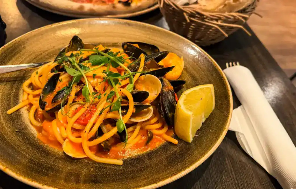 Seafood pasta with mussels, garnished with herbs and a lemon wedge on a dark plate.