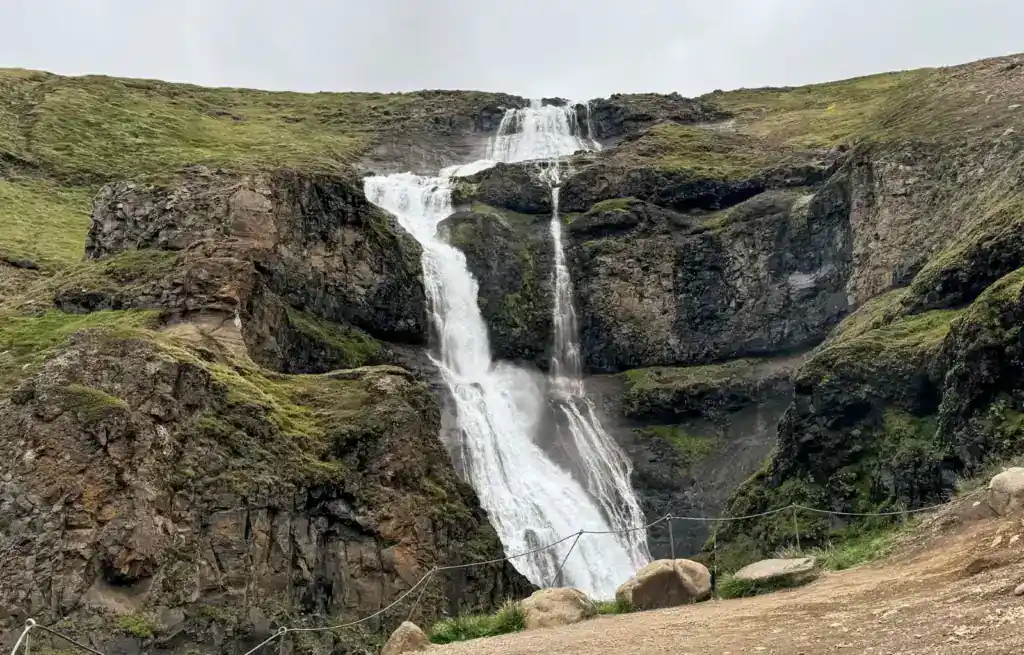 Majestic waterfall cascading down dark rocky cliffs with green moss and grass at the top and sides.