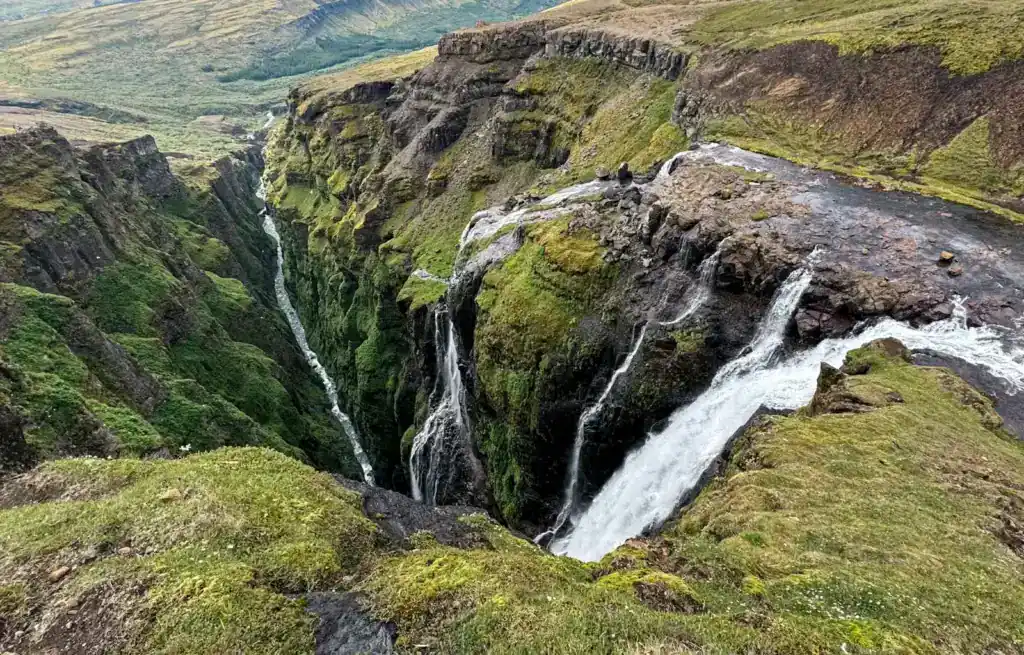 Waterfalls cascading into a deep green canyon with moss-covered rocks and lush vegetation.