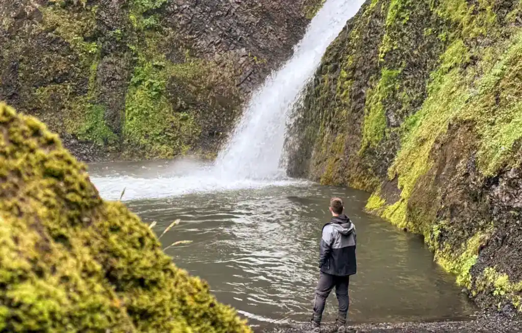 Person standing near a waterfall in a moss-covered canyon in Iceland.