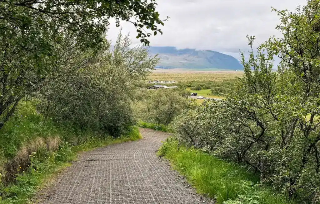Gravel trail winding through lush greenery with distant mountains under cloudy sky.