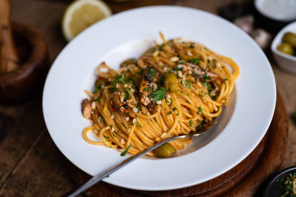 Nahaufnahme von Spaghetti mit eingelegten Sardinen, Pinienkernen, Oliven und frischer Petersilie – inspiriert von der italienischen Küche