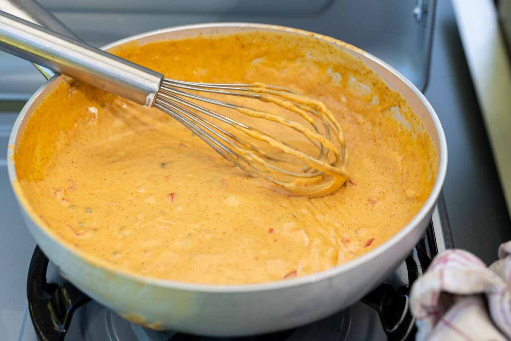 Cremige Chili Cheese Sauce mit Cheddar, grünen und roten Chilis in einer gusseisernen Pfanne