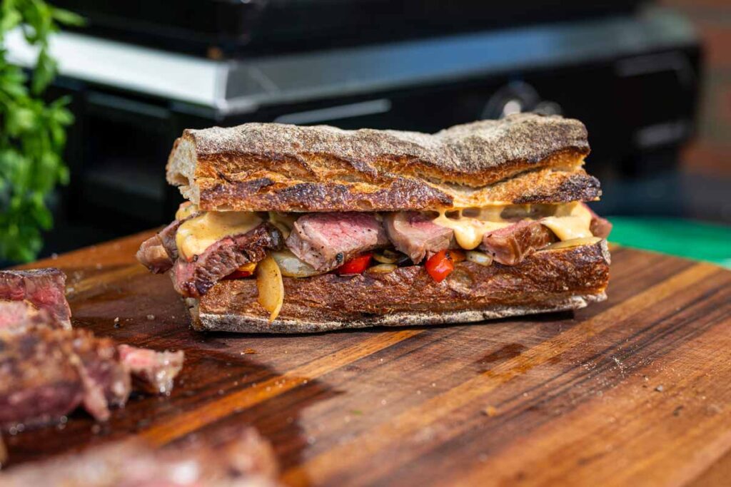 Angerichtetes Sandwich mit gegrilltem Ribeye Steak, cremiger Chili Cheese Sauce und geröstetem Gemüse