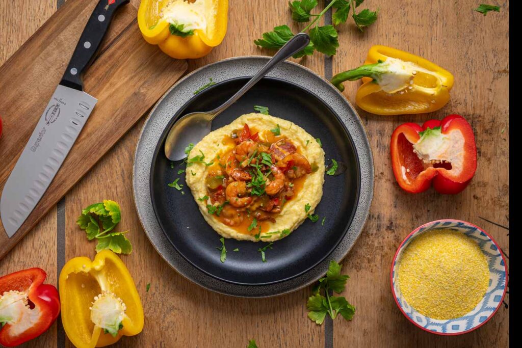 Detailaufnahme von Shrimp and Grits mit goldbraunen Garnelen, geschmolzenem Käse in der Maisgrütze und Röstaromen vom Bacon