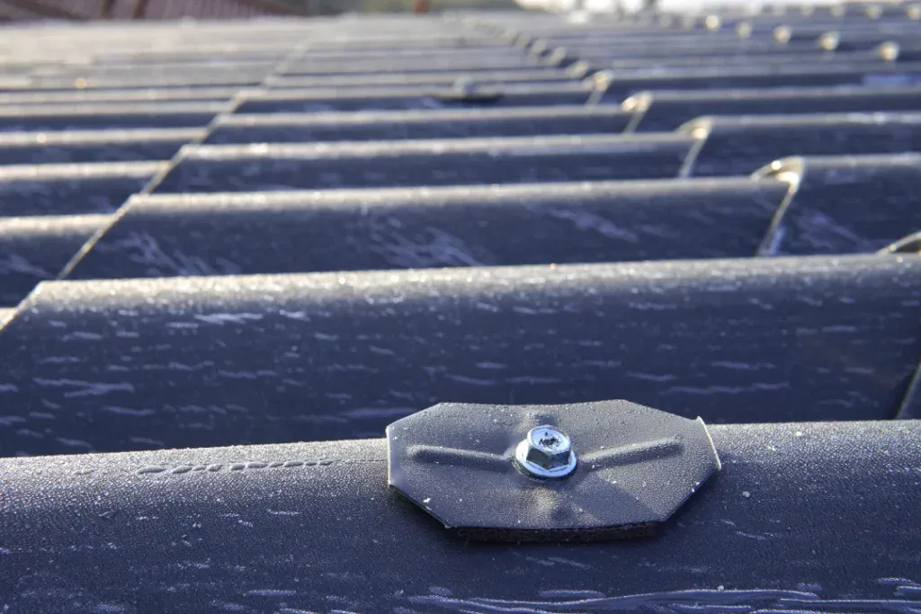 EPDM rubber roofing membrane close-up showing metal fixing clip and screw securing waterproof seam overlap