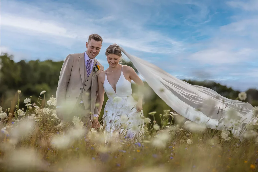 Wedding photograph of a couple walking through a field of summer flowers.