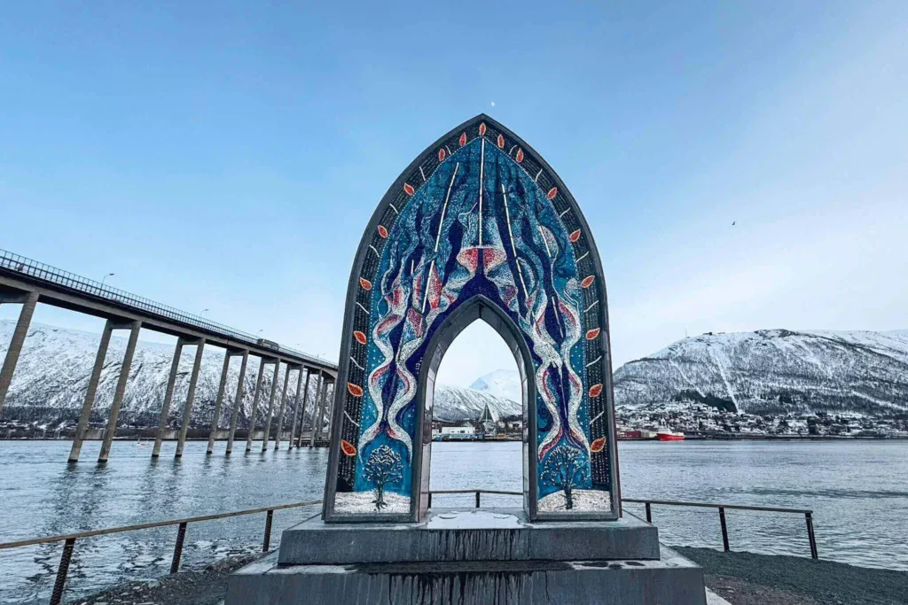 The Porten til Ishavet archway with the Tromso cathedral in the background framed by mountains on one side and a bridge on the other