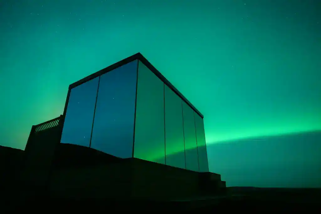Modern glass building with northern lights in the sky above it.