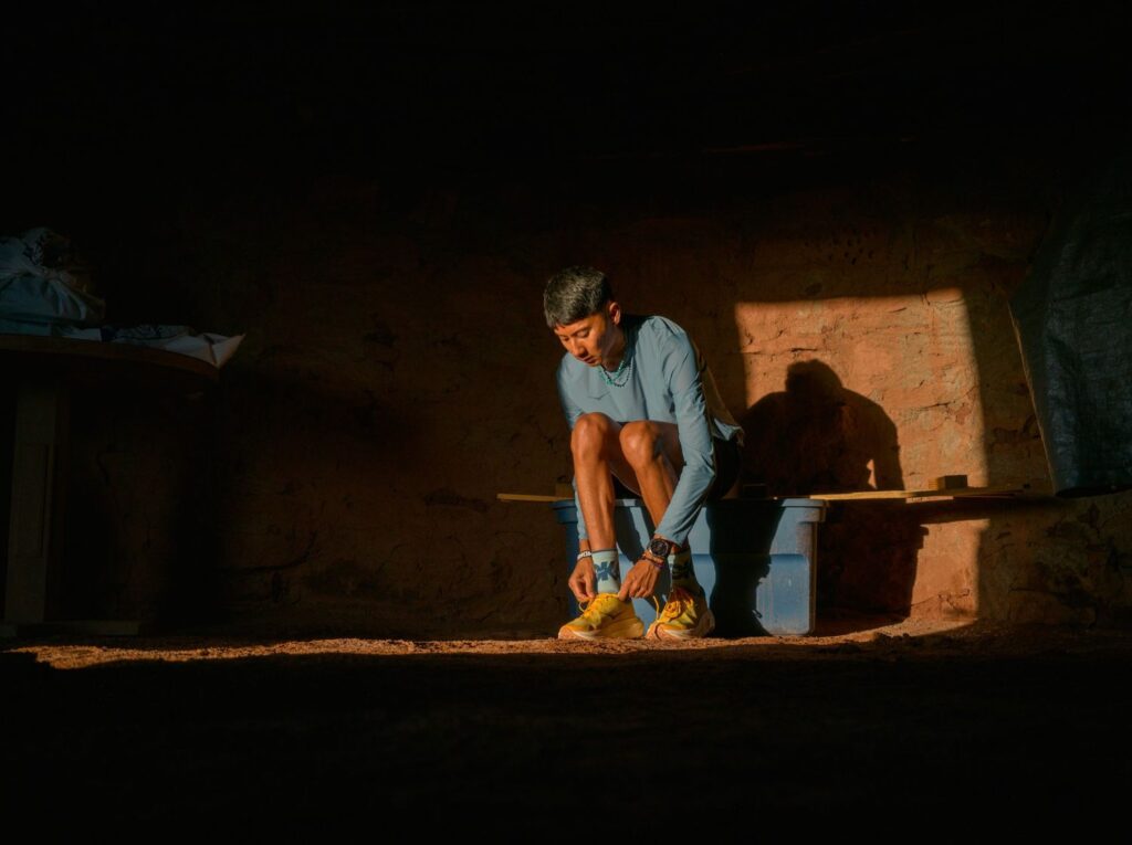 A photo of a man sitting on some rocks tying his shoelaces