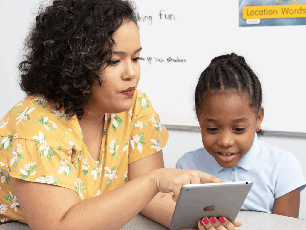 Teacher and young student looking at a tablet together in a classroom setting.