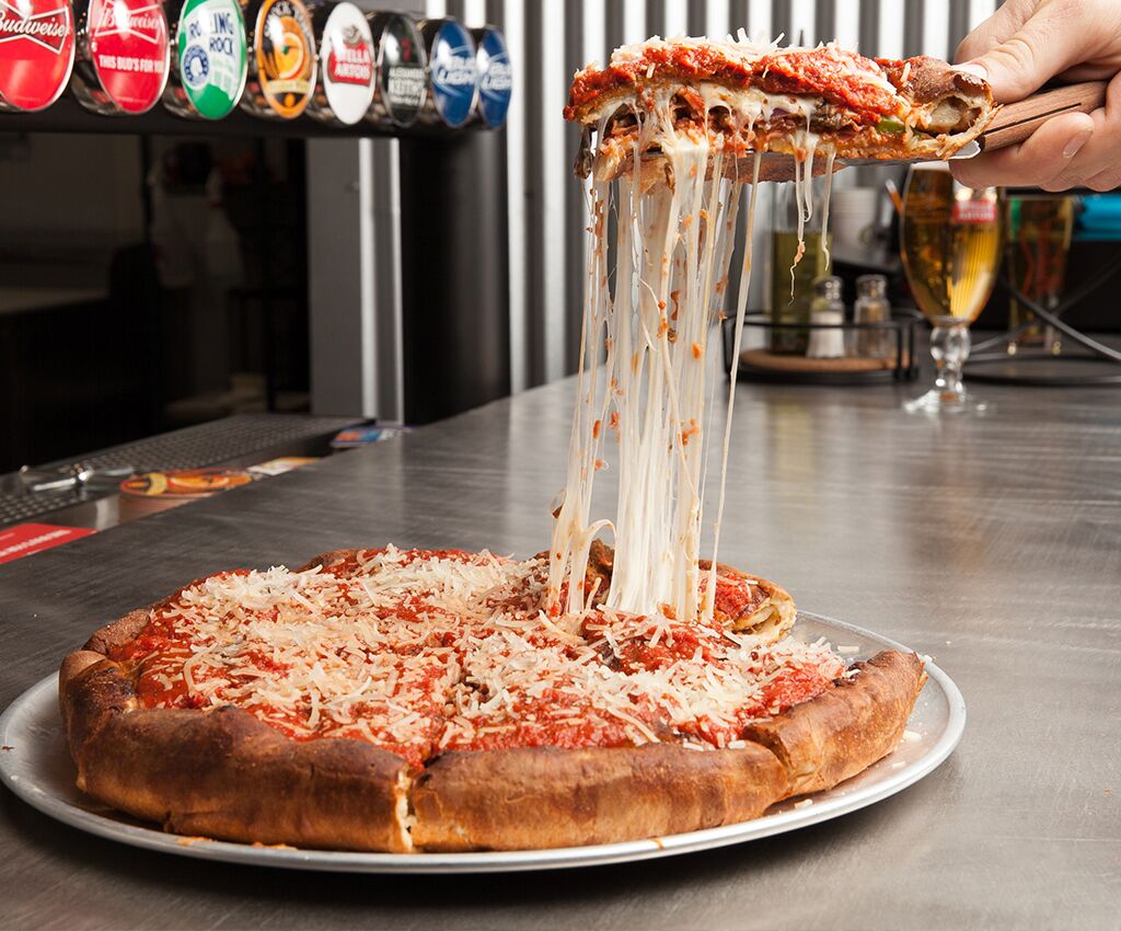 Chicago style deep dish pizza with a slice being lifted out of the pie and a long cheese pull string, with gluten free and vegan options for the best pizza in town!