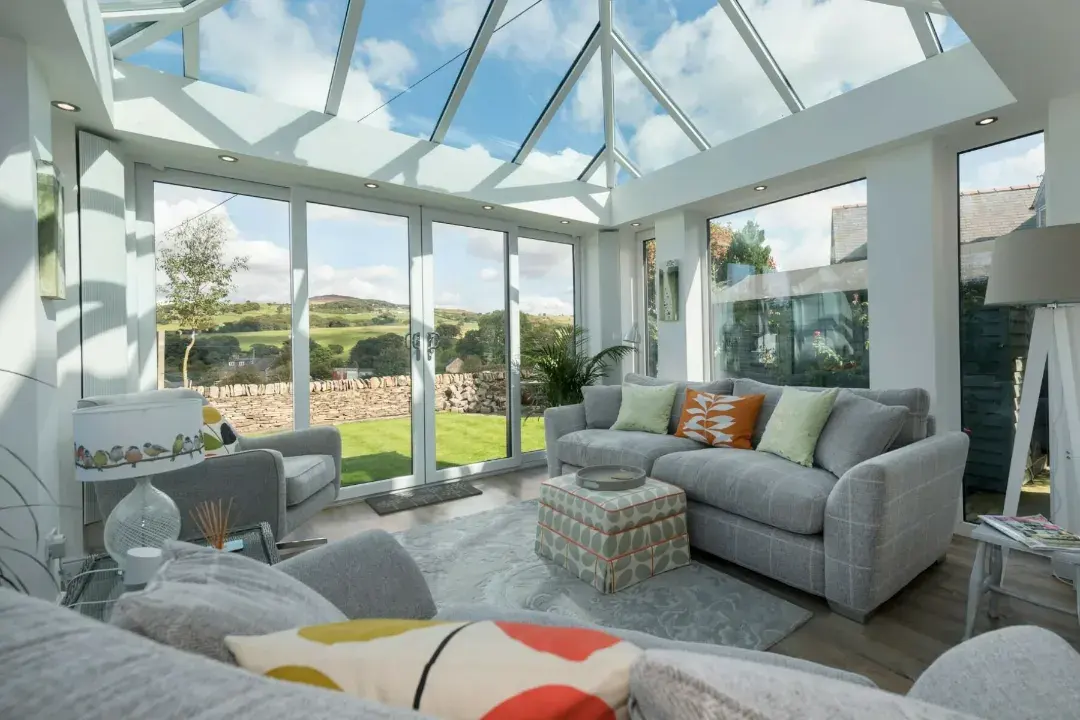 Bright conservatory lounge with a glass roof, white frames, garden doors and countryside views.