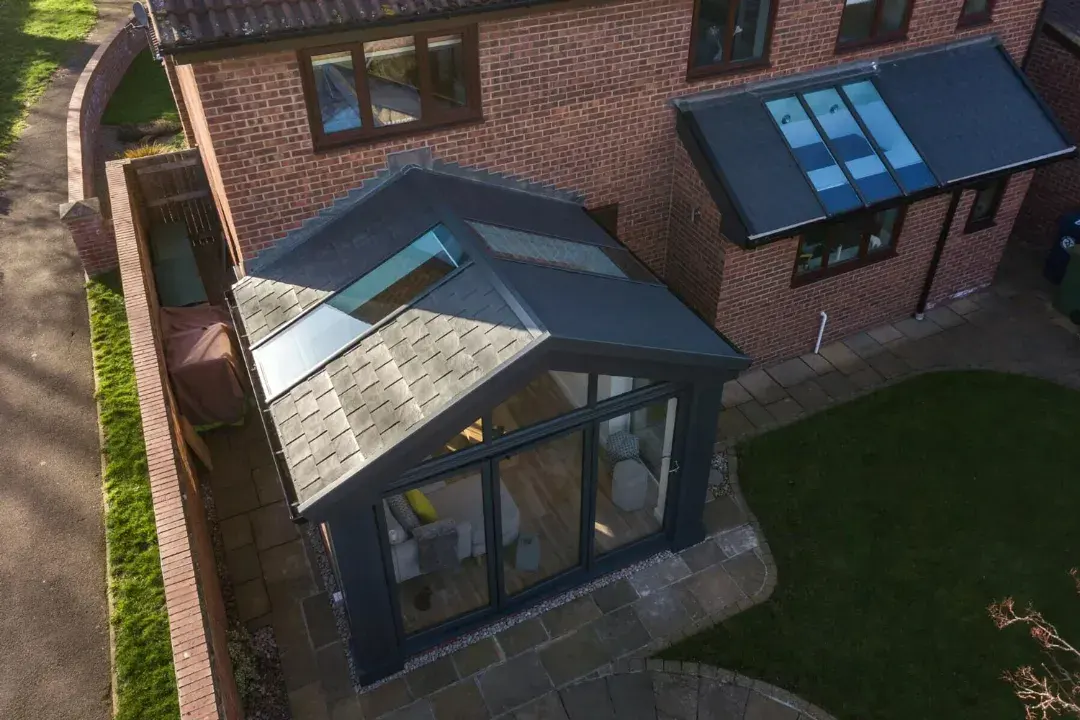 Aerial view of a tiled conservatory roof with roof windows, dark frames and a brick house extension.