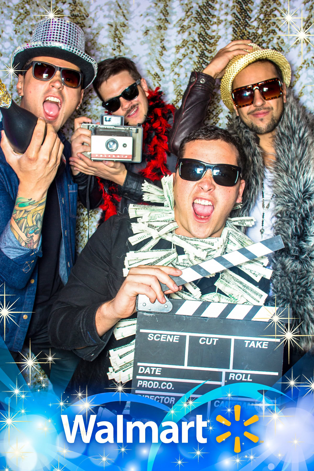 Four men wearing sunglasses and hats pose with props—a boombox and clapperboard—in a Walmart-themed photo backdrop.