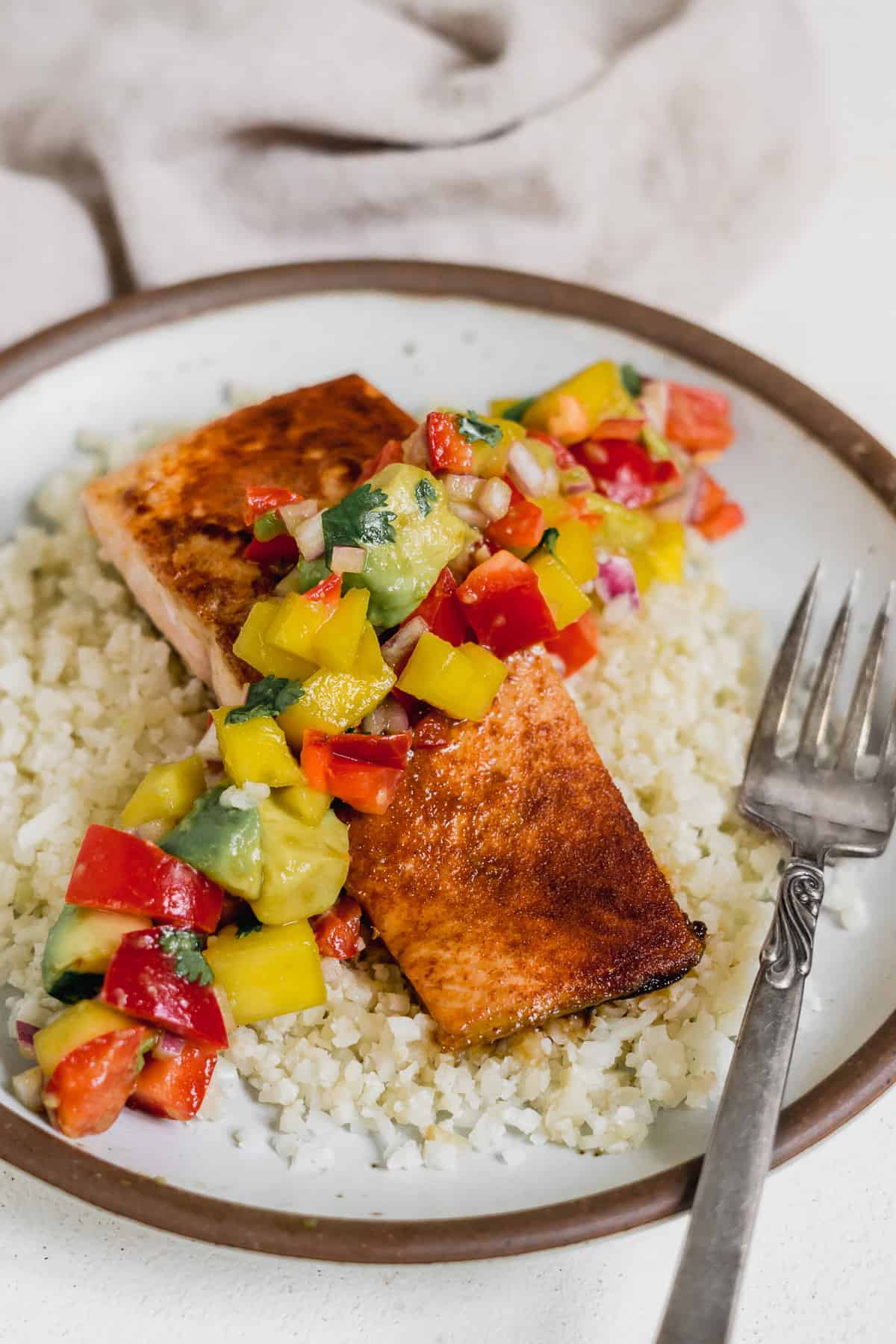 Brown plate with rice and seared salmon and a mango salsa.