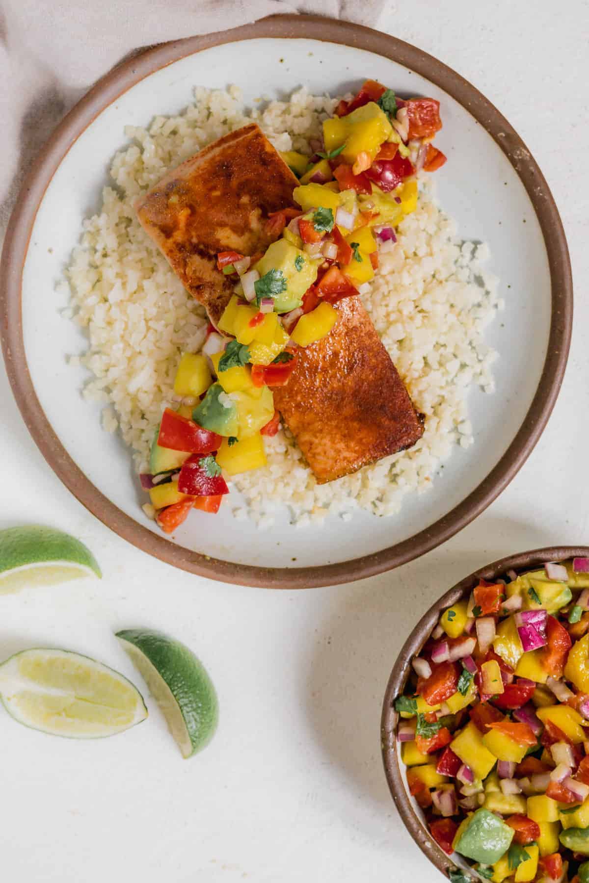 Overhead view of a grey plate with rice and salmon and avocado and mango salsa.