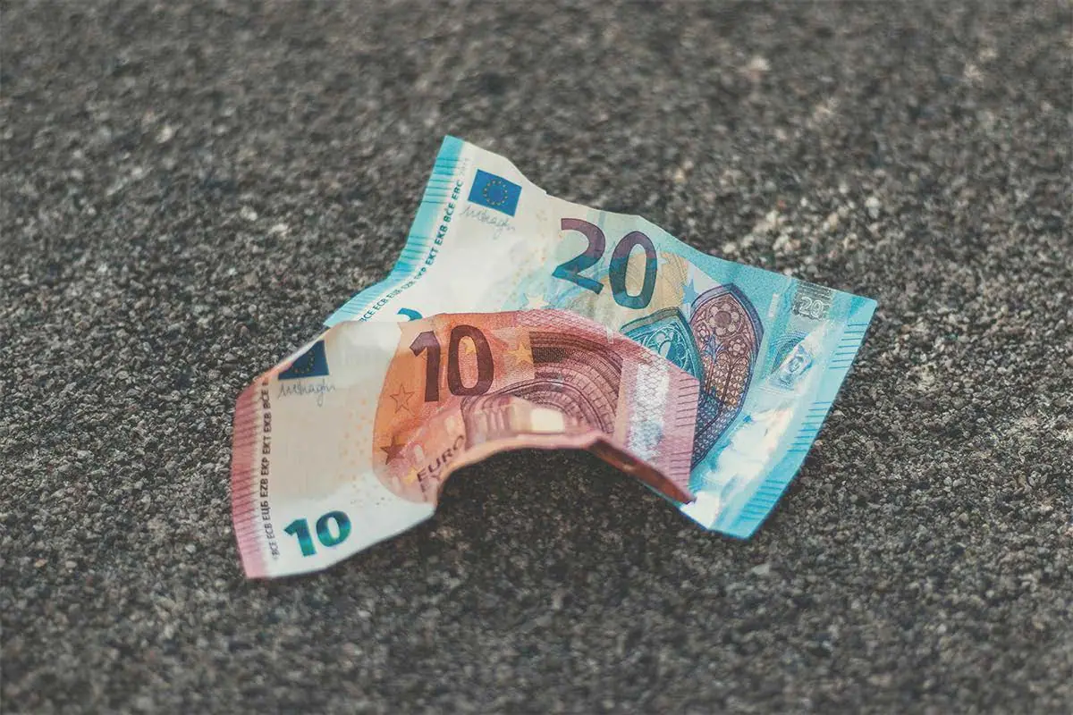 Zerknitterte 10- und 20-Euro-Banknoten liegen auf einem rauen Asphaltboden.