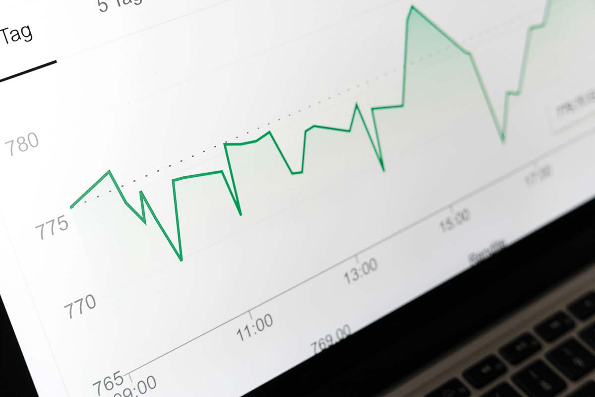 Laptopbildschirm zeigt Kursschwankungen eines Börsencharts mit grüner Linie im Tagesverlauf.