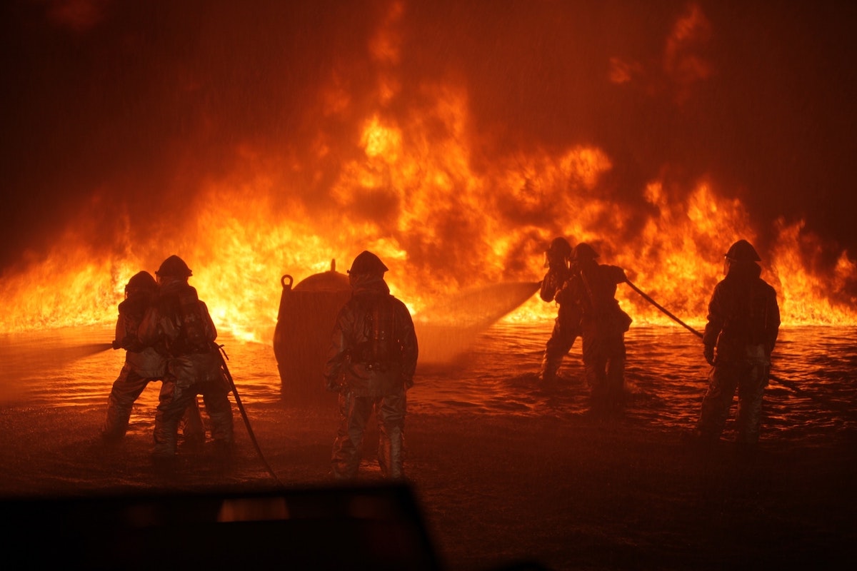 Feuerwehrleute löschen einen großen Brand mit Wasser in dunkler Umgebung.