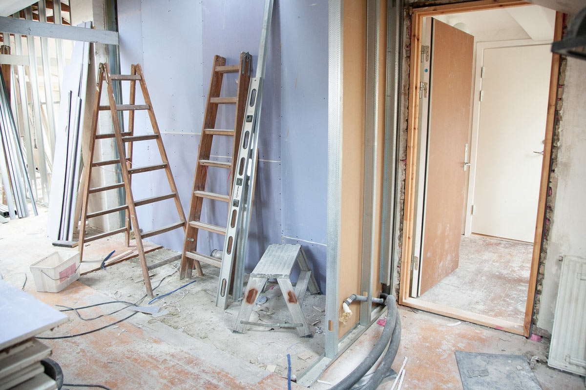 Baustelle eines Innenraums mit Leitern, Metallprofilen und offenen Türen, umgeben von Baumaterialien und Werkzeugen.