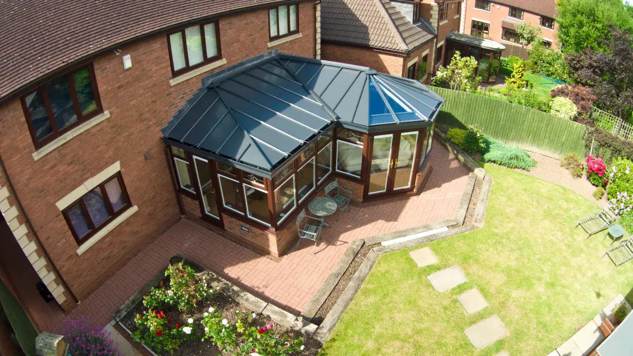 Aerial view of a brown framed conservatory with a solid roof, brick base and garden patio.