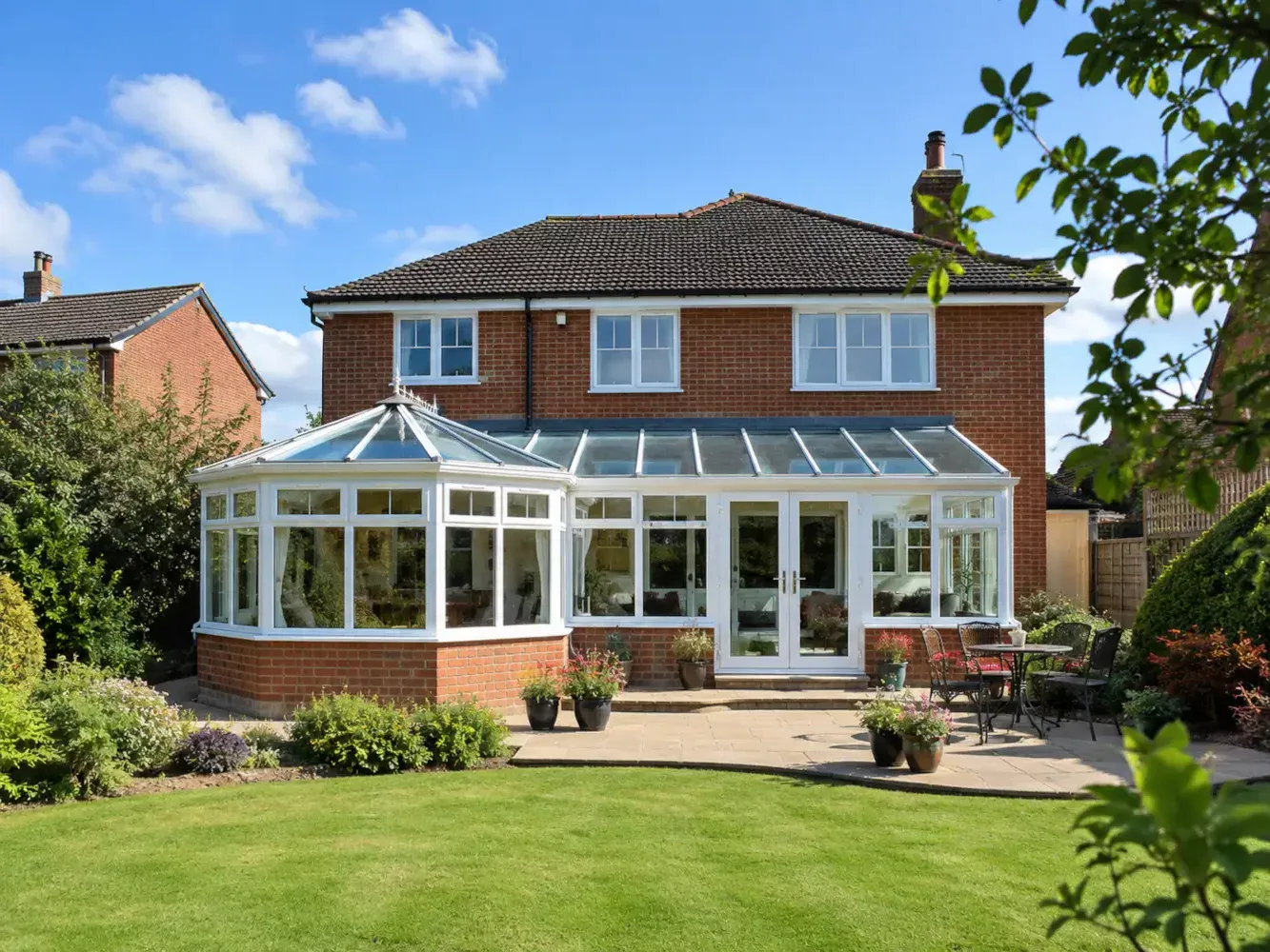 Combination conservatory with white frames, glass roof and garden view on a bright sunny summer day.