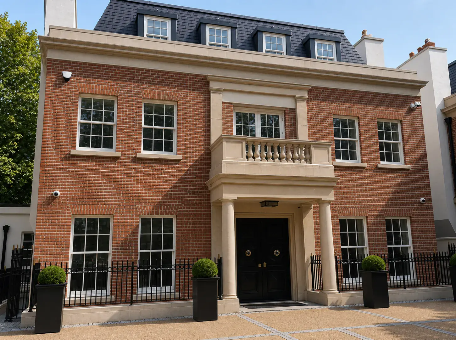 Elegant two-story brick house with symmetrical windows, a central balcony, black double doors, and potted plants.